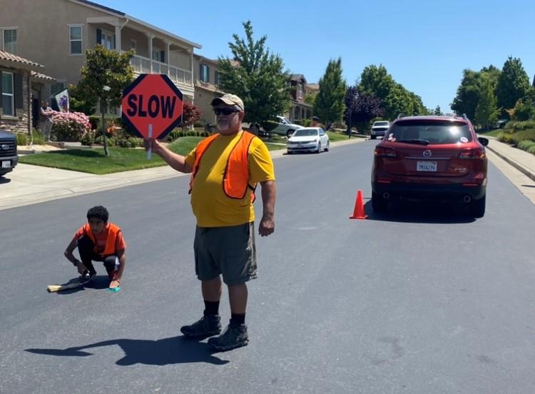 A safety volunteer holds a traffic sign while a boy scout installs a wildland access marker on a Rocklin street